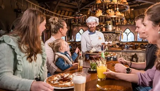 Zdjęcie przedstawiające stolik, przy którym rozmawiają goście restauracji z kelnerem.